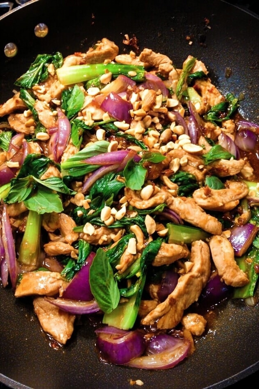 In a black wok, there is a colorful stir-fry with several layers; the base layer is made of chopped light green bok choy pieces and bright green leafy herbs spread evenly, above this are thin, light brown strips of cooked meat mixed with chunks of red onion that have a soft purple color, the top layer is sprinkled with small pieces of pale tan peanuts, adding texture. The wok has a wooden spatula resting on one side, and the food looks fresh and vibrant with a mix of green, purple, brown, and tan colors. photo taken with an iphone --ar 2:3 --v 7