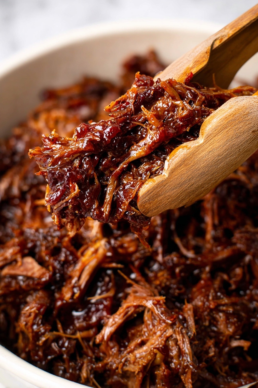 A close-up view of shredded dark brown meat with a glossy, moist texture, held by a wooden pair of tongs in the center. The meat looks tender with some red and black spices visible. The background shows more shredded meat in a white dish against a white marbled surface. The focus is sharp on the meat held by the tongs, while the background is blurred, creating a rich and inviting look. photo taken with an iphone --ar 2:3 --v 7