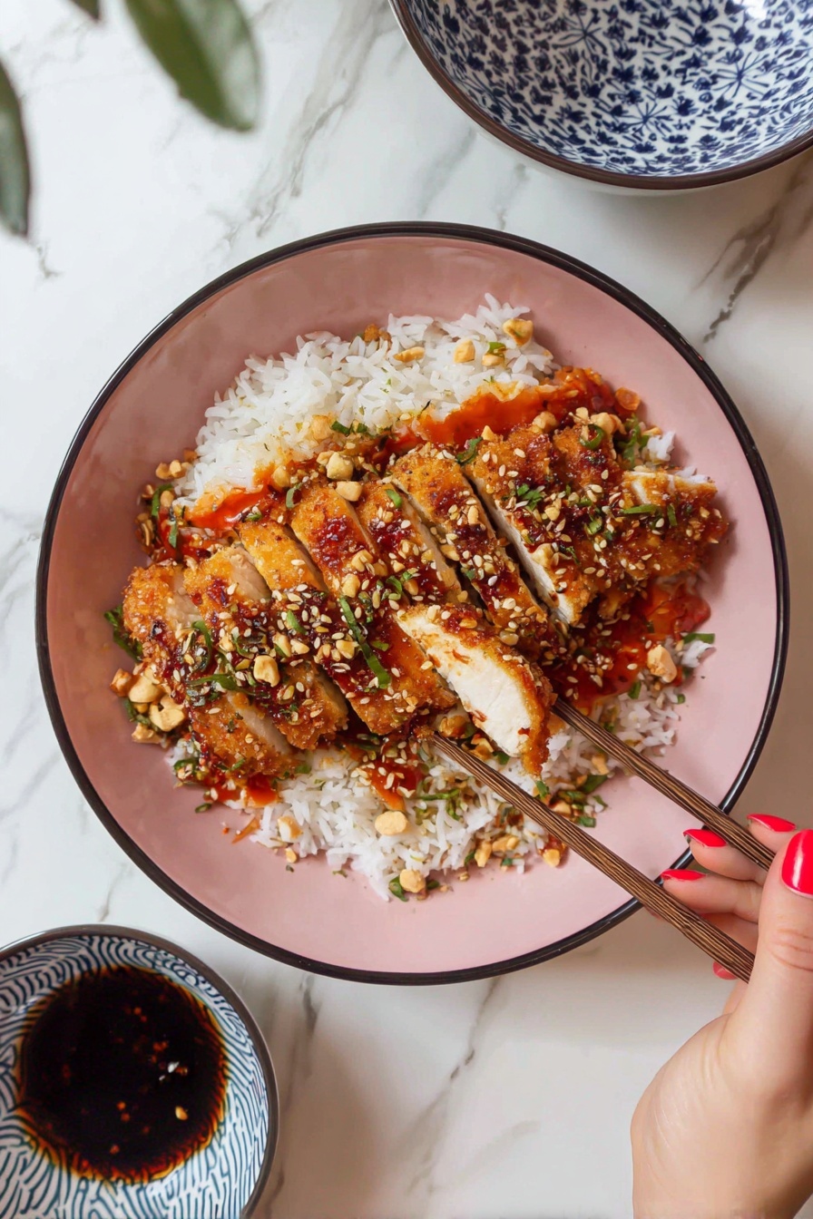 A pink bowl filled with white rice at the bottom, topped with golden brown crispy sliced chicken pieces arranged neatly in the center. The chicken is decorated with green herbs, chopped nuts, and sesame seeds, with a red-orange sauce pooling around the rice. A woman's hand with red nail polish is holding wooden chopsticks picking up one slice of chicken. The bowl sits on a white marbled surface, beside a small white bowl with blue patterns holding a dark sauce and some white flowers on the side. photo taken with an iphone --ar 2:3 --v 7