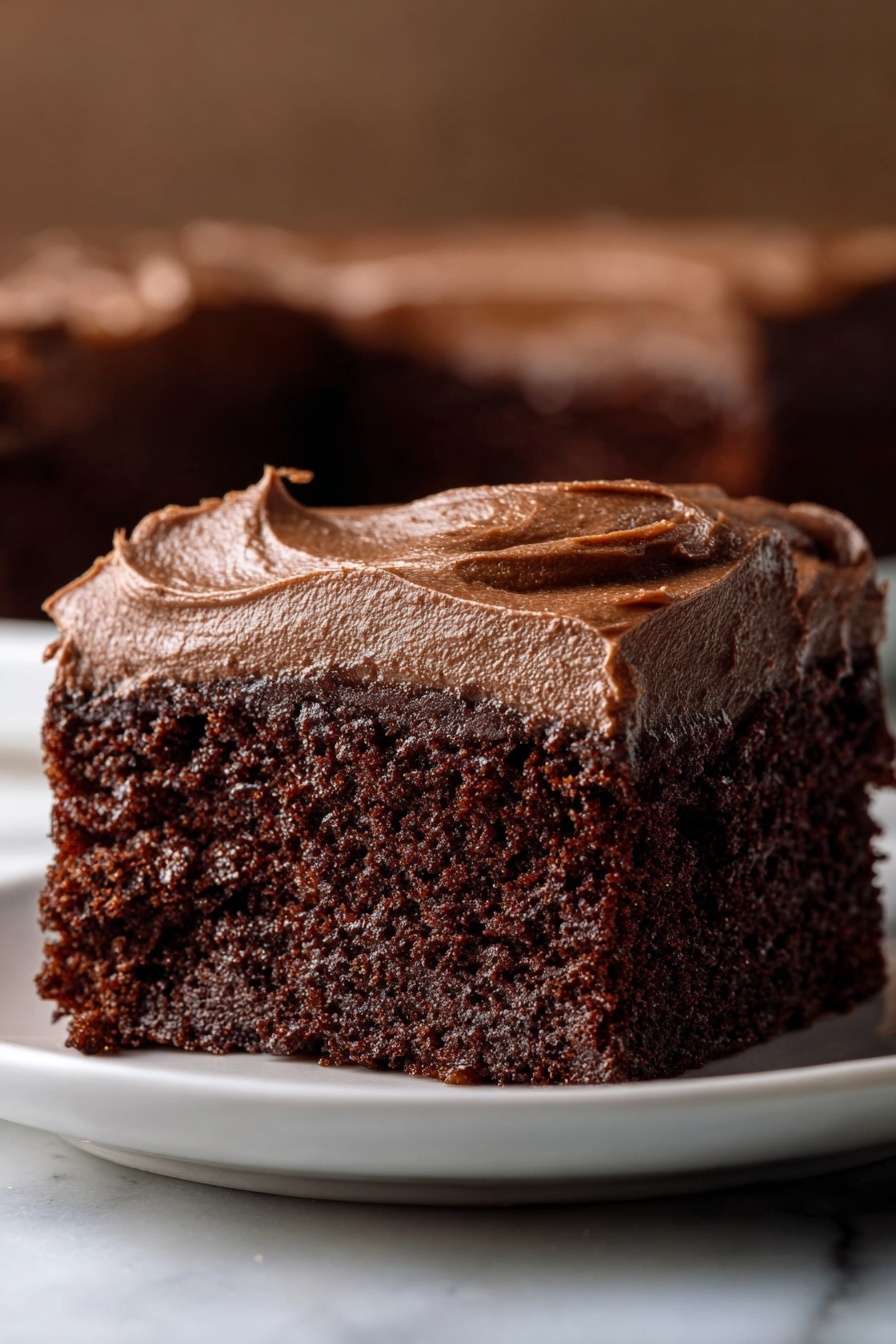 The image shows a close-up of a single square piece of chocolate cake on a white plate, placed on a white marbled surface. The cake has two main layers: a thick, moist dark brown chocolate base with a soft, crumbly texture, and a smooth, thick layer of darker chocolate frosting spread evenly on top. The frosting has a glossy and creamy look with small swirls and peaks around the edges, adding texture. In the background, the image is blurred but has a warm, dark brown color. Photo taken with an iphone --ar 2:3 --v 7