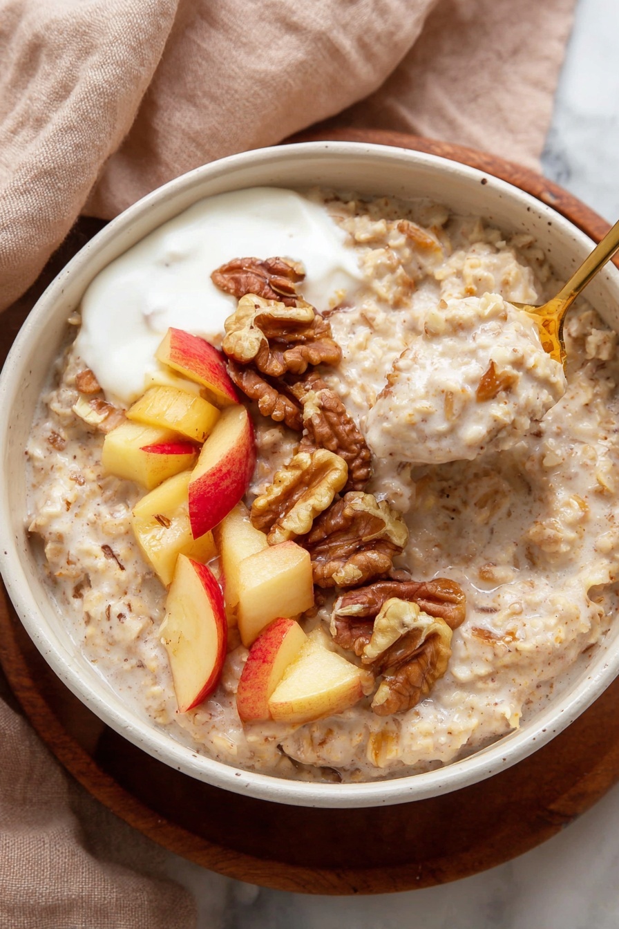 A bowl of creamy oatmeal forms the base layer, light beige in color with a thick, slightly textured surface showing oats and small chunks of apple. On top, there is a neat row of walnut halves, dark brown and light tan, curving along one side. Next to the walnuts, a dollop of white yogurt sits, smooth and slightly glossy. Bright red and yellow apple pieces with a light sprinkle of cinnamon are placed near the yogurt, their colors bright and fresh. A gold spoon is lifting a portion of oatmeal, apple pieces, walnut, and yogurt from the bowl. The bowl itself is white with tiny dark speckles, placed on a white marbled surface. Photo taken with an iphone --ar 2:3 --v 7
