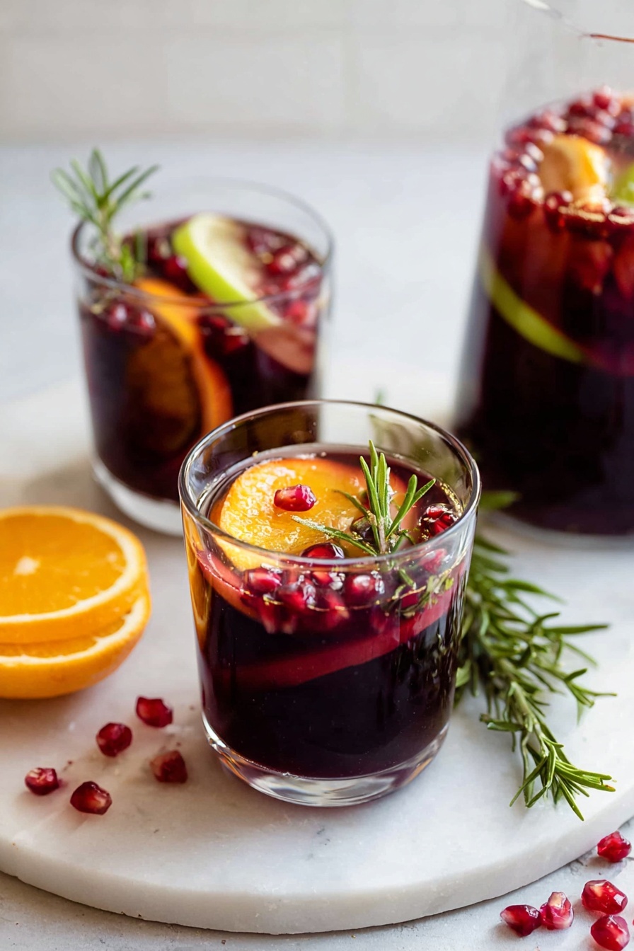 Two clear glasses sit on a white marbled surface, each filled with a deep red liquid. Each glass holds slices of bright orange and light green fruit floating on top, along with small red pomegranate seeds scattered inside the drink and on the surface. One glass has a green rosemary sprig standing upright, adding a touch of texture. There are more pomegranate seeds scattered around the surface near the glasses, and a larger rosemary sprig lies flat beside one glass. The background is soft and out of focus. photo taken with an iphone --ar 2:3 --v 7