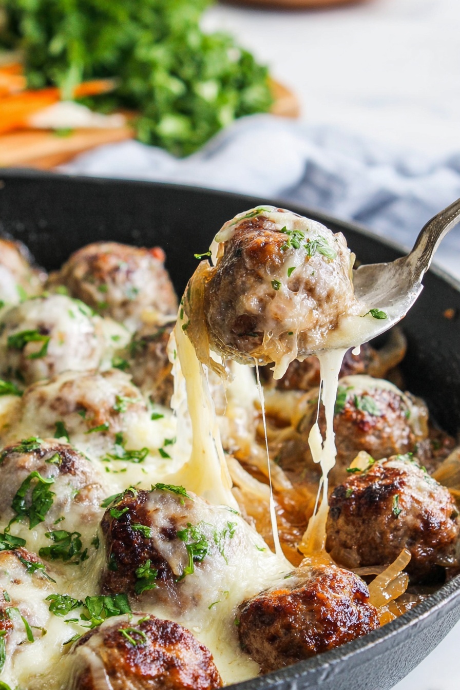 A close-up view of a black pan filled with browned meatballs covered in melted, stretchy white cheese. Underneath the meatballs, there are cooked onions with a soft, translucent texture. Small bits of chopped green herbs are sprinkled on top of the cheese and meatballs, adding a fresh touch. A metal spatula lifts one meatball, showing the pull of the melted cheese connecting it to the other pieces. The background shows blurred fresh green herbs on a white marbled surface. photo taken with an iphone --ar 2:3 --v 7