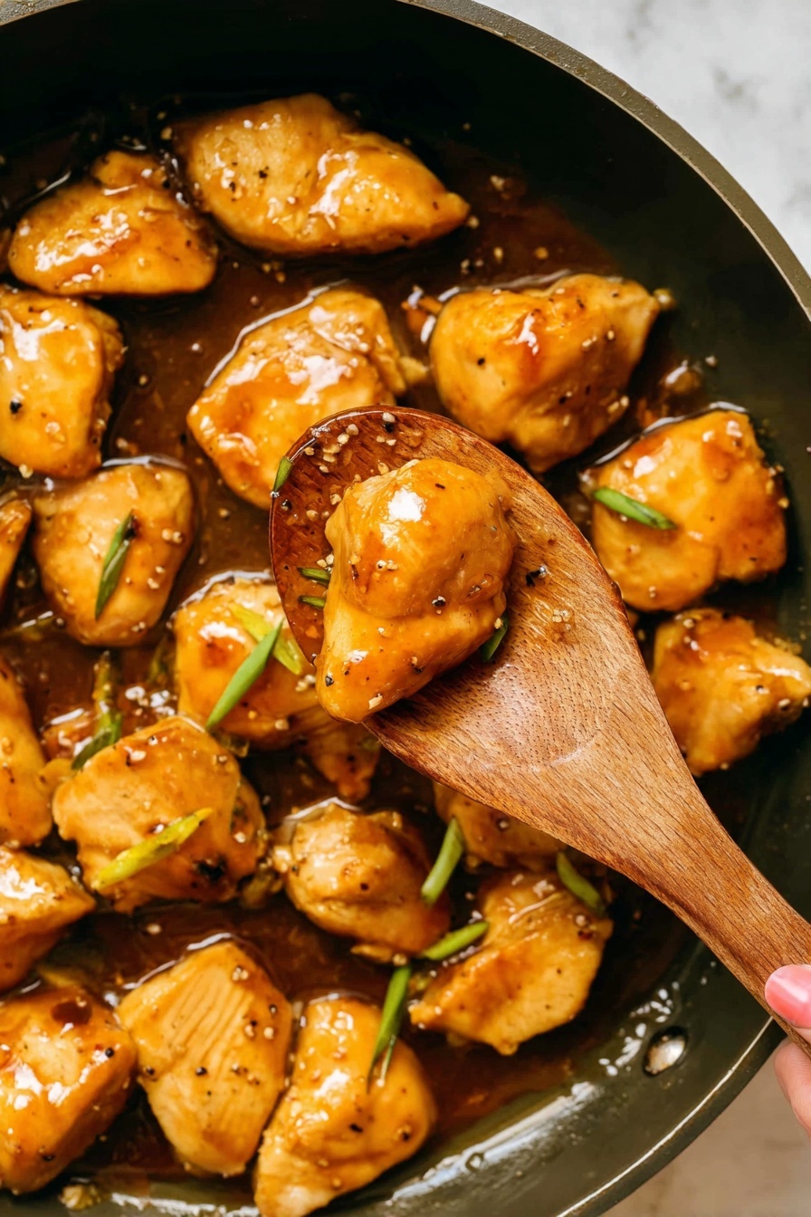 The image shows golden brown chicken pieces cooked in a shiny sauce, with some green onion slices mixed in. Two chicken pieces glisten on a wooden spoon in the center, surrounded by more chicken pieces in the dark pan below. The sauce looks smooth and oily, coating the chicken well. The colors are warm, with the chicken having a light brown exterior and a juicy texture visible. The pan's surface is dark, making the chicken and sauce stand out clearly. photo taken with an iphone --ar 2:3 --v 7