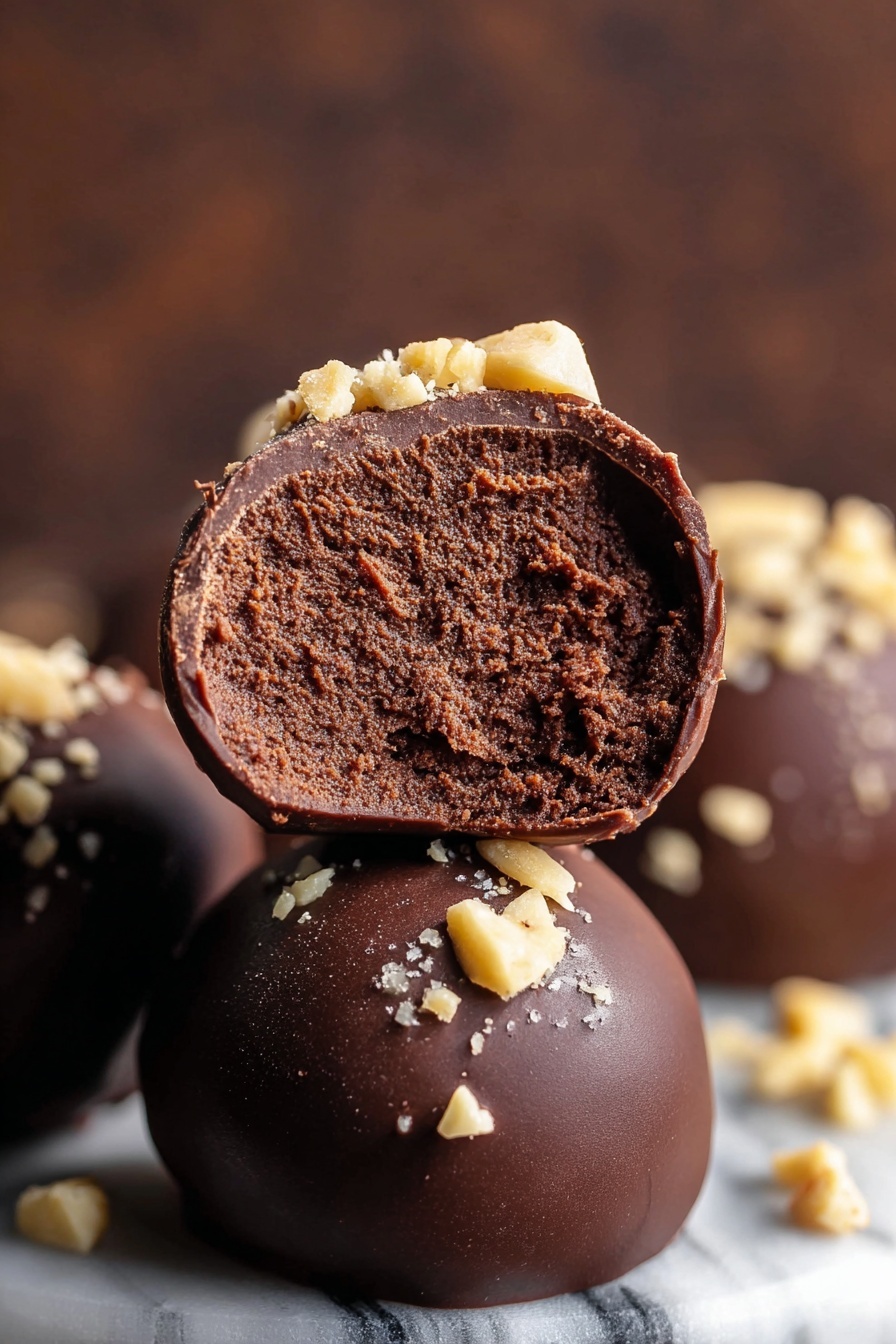 Seven round chocolate balls are arranged closely in a white bowl on a white marbled surface. Each ball has a smooth, dark brown chocolate coating with a slight shine, and they are topped with small, light tan chopped nuts scattered unevenly on top. The balls have a soft, smooth texture with subtle curves, making them look rich and fresh. The photo taken with an iphone --ar 2:3 --v 7