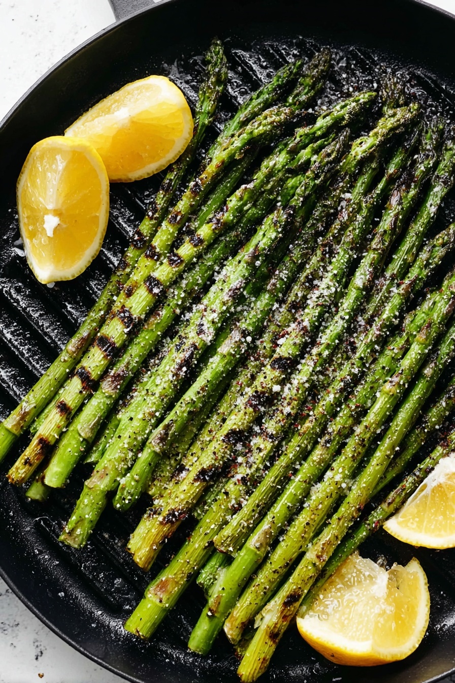 A black round grill pan holds a single layer of long, bright green asparagus spears arranged side by side, some showing light char marks and grill lines. Coarse white salt and black pepper flakes are scattered over the asparagus. There are three lemon wedges placed on the top right and bottom left edges of the pan, each with visible grill marks and a glossy texture. The pan rests on a white marbled surface. Photo taken with an iphone --ar 2:3 --v 7