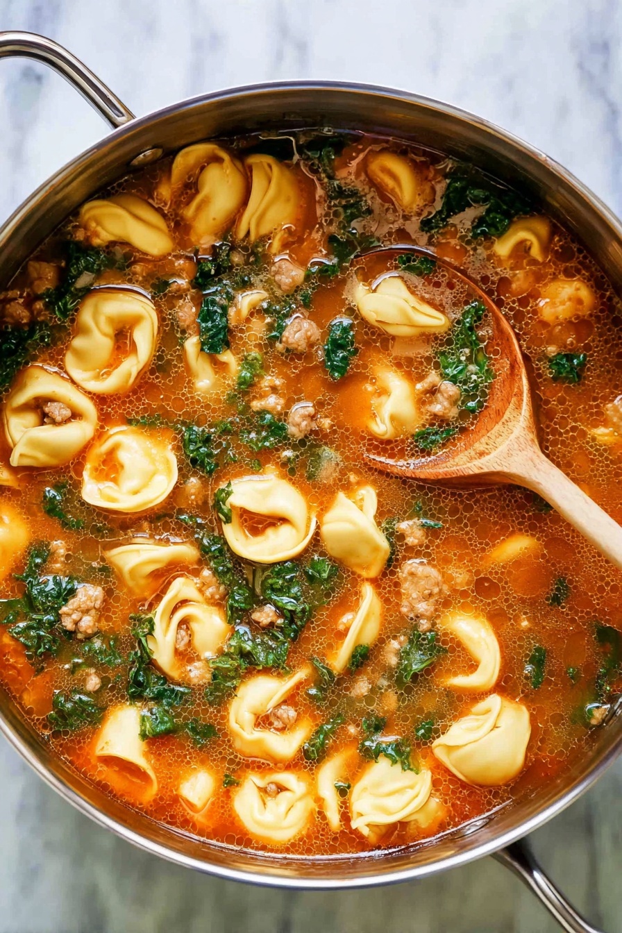 A close-up top view of a silver pot filled with tomato-based soup showing three main layers: the top layer is a mix of pale yellow tortellini pasta with smooth curved edges, bright green leafy kale pieces scattered evenly, and some light brown cooked meat bits. The middle layer is a rich orange-red broth with small oil bubbles and tiny herbs floating in it, giving a smooth and slightly shiny texture. At the bottom, partially submerged in the soup, a wooden spoon with a dark curved bowl and pale wooden handle is visible, slightly stirring the soup. The pot rests on a white marbled surface. Photo taken with an iphone --ar 2:3 --v 7