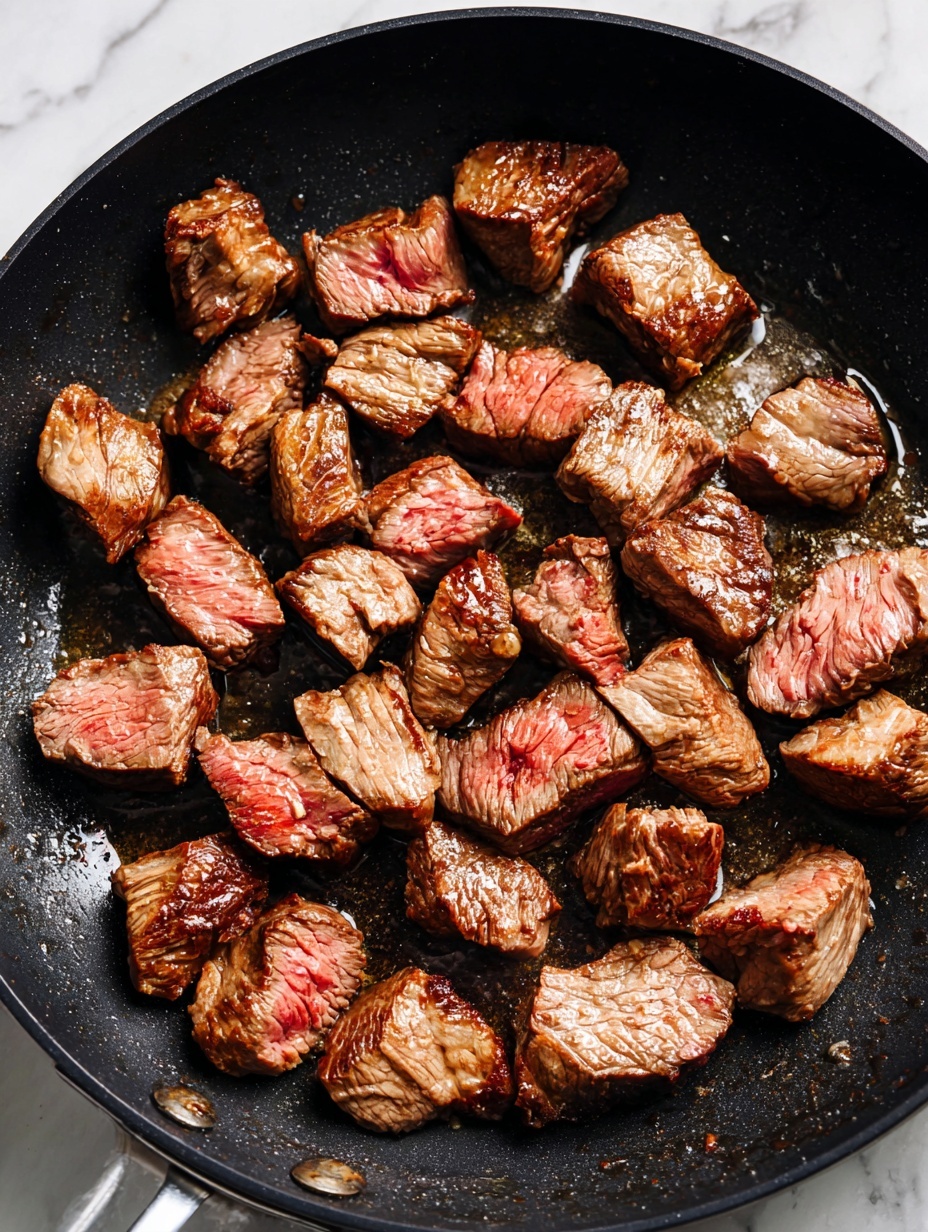 Chunks of browned beef are scattered in a black pan. Each piece shows a mix of deep brown seared surfaces with hints of pink on some edges, giving a rough textured look to the meat. The pan bottom appears oily and shiny with some small juices around the beef pieces. The colors mostly range from dark brown to light brown with touches of reddish-pink. photo taken with an iphone --ar 2:3 --v 7