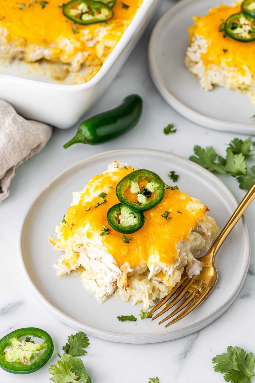 A white plate holds one square piece of a cheesy casserole with three visible layers: the bottom layer is creamy white, the middle layer is shredded chicken or similar light meat, and the top layer is melted bright orange cheese with small green cilantro bits sprinkled on it. Two green jalapeño rings sit on top of the cheese. A gold fork is placed on the plate with the casserole, resting on the plate’s edge. Nearby on a white marbled surface, there is a white baking dish with more casserole showcasing the same three distinct layers and melted cheese topping. Fresh cilantro leaves and a few jalapeño rings are scattered on the table, and part of a sliced avocado is visible in the corner. Photo taken with an iphone --ar 2:3 --v 7